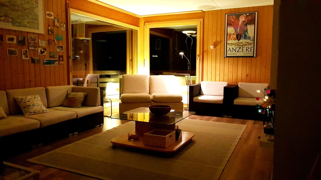 Le salon de l'appartement en soirée : boiseries, canapés et affiche d'Anzère